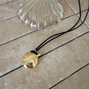 Detailed view of an oval gold perfume bottle pendant on a black cord necklace