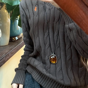 Detail of amber resin oval pendant with silver frame on a black adjustable cord