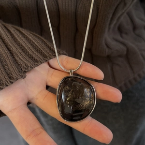 Close-up of irregular dark brown resin pendant on silver chain over a cozy knit sweater