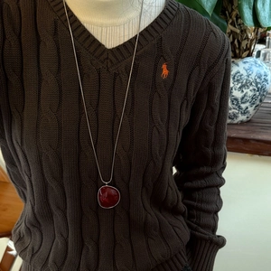 Close-up of deep red resin circular pendant with silver edge on sweater chain