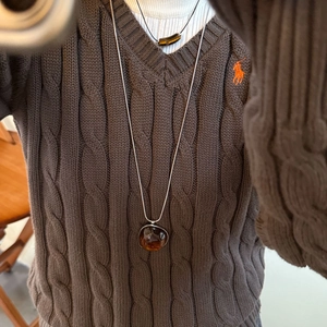 Detail of a vintage amber resin circular pendant on a silver snake chain over a sweater