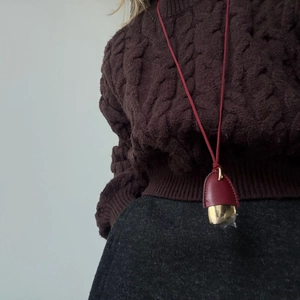 Close-up of red leather and gold metal pinecone pendant necklace on cable knit sweater