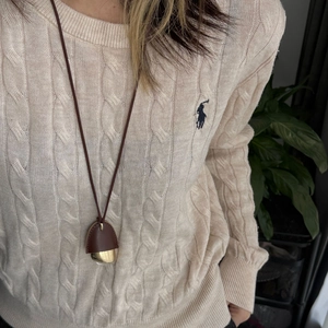 Detail of an acorn pendant with brown leather cap and gold metal base on a beige sweater