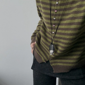 Detail of pine cone pendant on leather cord necklace worn with striped knit cardigan