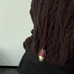 Close-up of leather key bell pendant necklace with gold hardware on knit sweater