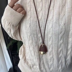 Detailed view of acorn pendant with brown leather and golden metal on beige knit sweater
