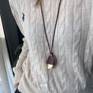 Close-up of a brown leather and gold nut pendant necklace on a beige knitted sweater