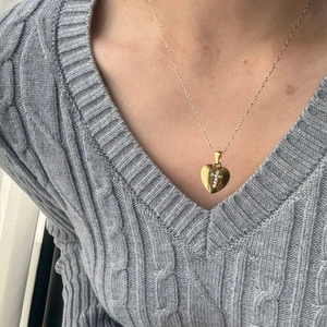 Dettaglio della collana a cuore dorata con croce di cristallo su maglione a trecce