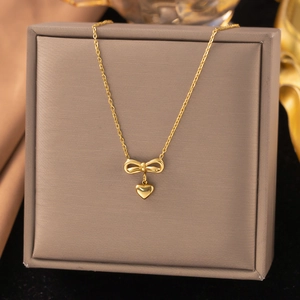 Détail du collier doré en acier inoxydable avec pendentif nœud et cœur sur écrin
