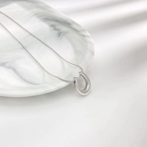 Minimalist silver horseshoe U-pendant snake chain necklace on a white marble tray