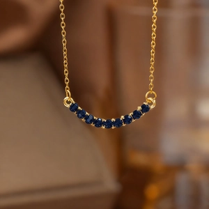 Elegant 18K gold smile necklace with curved dark blue gemstones in minimalist style