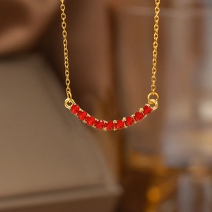 Golden curved necklace featuring eleven vibrant red crystals in a horizontal arch design
