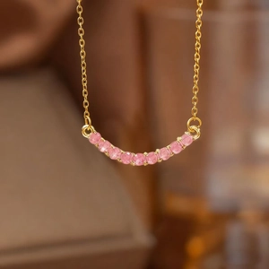 Detailed view of a gold curved bar pendant set with sparkling pink round gemstones