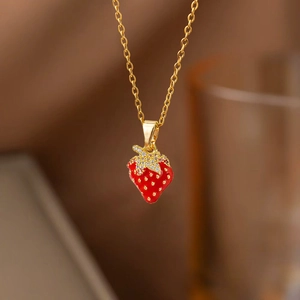 Détail d'un pendentif fraise en émail rouge avec feuilles en zircon et chaîne dorée brillante