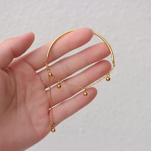 Close-up of gold titanium steel bracelet with tassels and beads held by hand