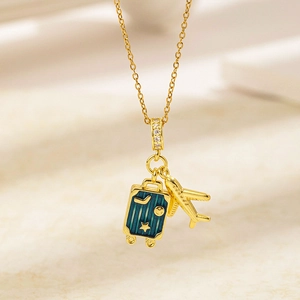 Détail du collier voyage globe doré avec un pendentif valise et un petit pendentif avion