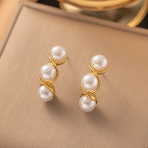 Macro detail of gold wavy earrings featuring three white pearls on a brushed metal background