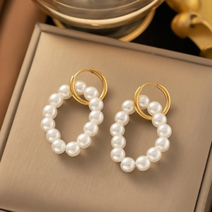 Detail of geometric pearl hoop earrings with golden finish on a champagne metal base
