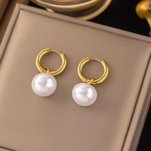 Elegant gold geometric hoop earrings with polished white pearl pendants on leather jewelry tray