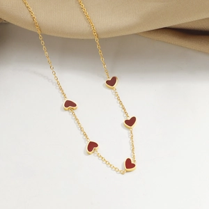 Collar minimalista de oro con cinco colgantes de corazón rojo sobre fondo de raso champán