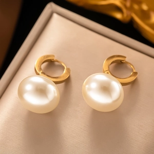 Detail of golden huggie earrings with lustrous round white pearls on beige leather padding