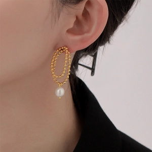 Macro detail of gold bead chain earrings with dangling pearl on a model's ear