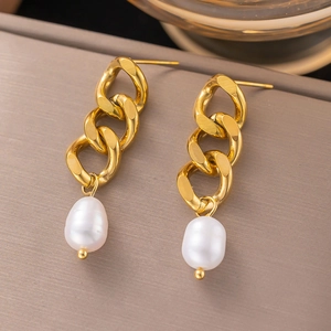 Detail of gold chain link earrings featuring white baroque pearls on a textured surface