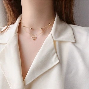 Primer plano de collar de doble capa dorado con colgante de corazón y cuentas en modelo