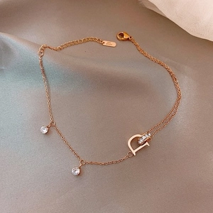 Detalle de un collar de oro rosa con colgante D de cristal sobre un fondo de seda suave
