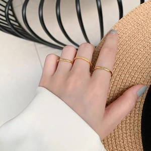 Three minimalist gold stacked rings on a model hand with a straw hat and soft lighting