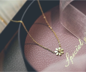 Detail shot of golden daisy pendant with delicate cross chain on red leather box