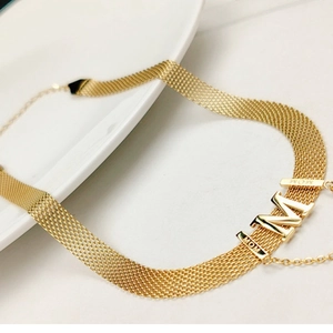Detail of gold woven mesh necklace with M letter pendant and MOM engraving on the band