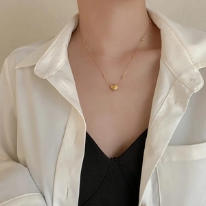 Minimalist gold heart pendant necklace with beaded chain on female model wearing white shirt
