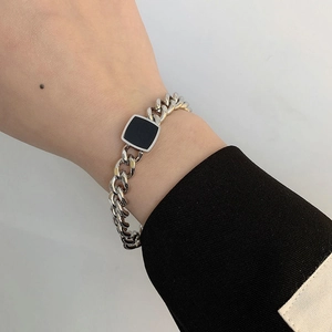 Detail of chunky silver Cuban chain bracelet with black square element on model wrist