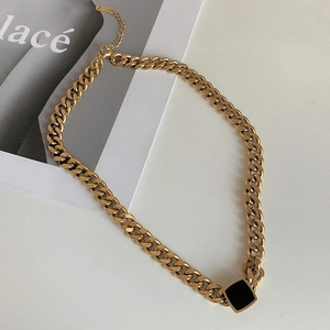 Detail of chunky gold chain necklace with square black pendant on fashion magazine background