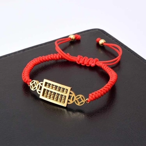 Detail of red braided rope bracelet featuring golden abacus and lucky coin charms