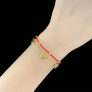 Detail of red braided cord bracelet with gold beads and heart charms on a wrist