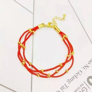 Detail of red braided cord bracelet with gold beads, lobster clasp and extension chain