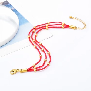 Detail of multi-layer red braided rope bracelet with gold beads and lobster clasp closure