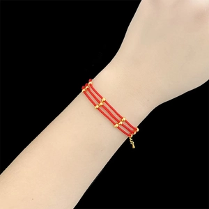 Detailed view of triple-layered red braided rope bracelet with round golden beads