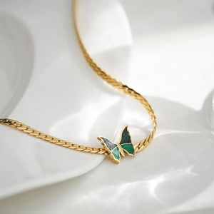 Detail of a golden snake chain necklace with a green enamel butterfly pendant in a ceramic tray