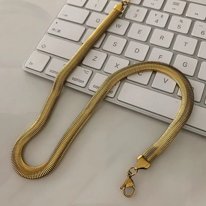 Detailed macro view of a flat gold snake bone chain resting on a white keyboard surface