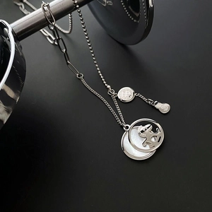 Macro detail of silver layered necklace with white mother of pearl and dollar sign charms