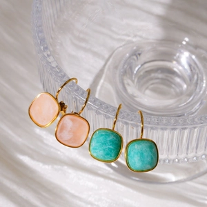 Detailed macro view of square natural stone earrings on textured glass with gold hooks