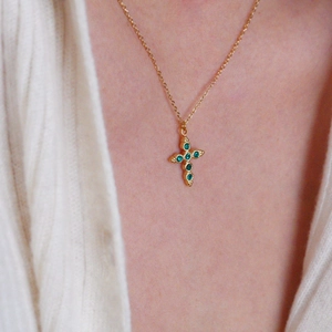 Cross necklace in gold plating with green gemstones shown on a female model