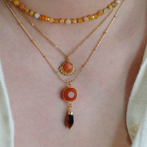 Close-up of triple-layered gold necklaces featuring orange stones and a water drop crystal