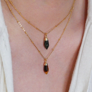 Close-up of double-layer gold necklace featuring tiger eye stone and hexagonal pendants