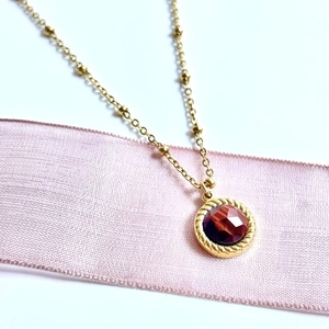 Detailed close-up of 14K gold satellite chain necklace with a red faceted stone pendant