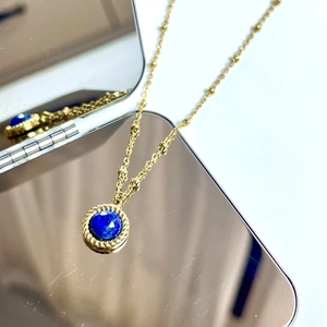 Detail of blue lapis stone pendant with gold rope edge and chain on mirror surface