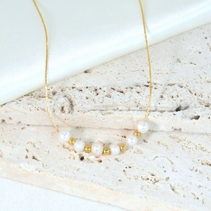 Elegante natuurlijke parelketting met gouden stalen kralen op witte zijden stof